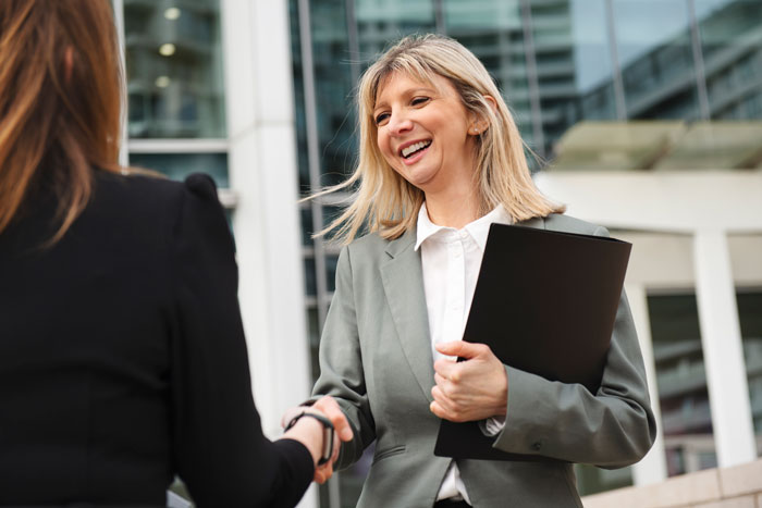 Professional career coach smiling and shaking hands outdoors, offering tips to ace interviews and land dream jobs.