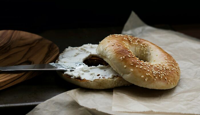 Sesame seed bagel with cream cheese spread on parchment paper, highlighting foods that go bad quickly.