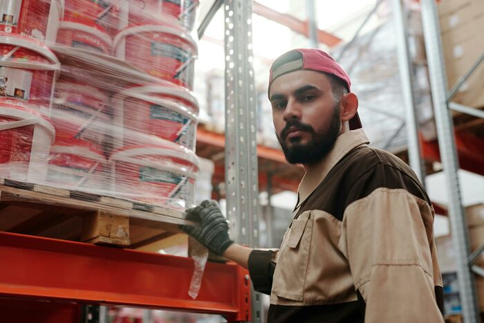 Warehouse worker in uniform organizing products on shelves, illustrating items cashiers may judge customers for buying.