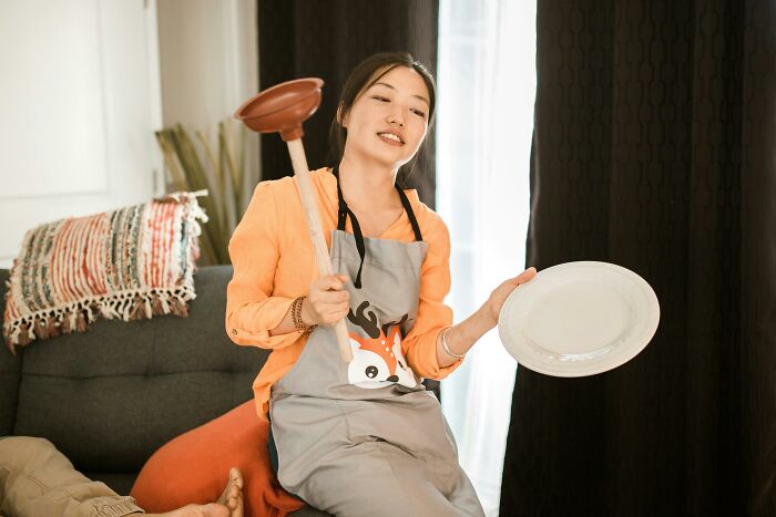 Woman in apron holding a plunger and plate, representing common things cashiers judge customers for buying.