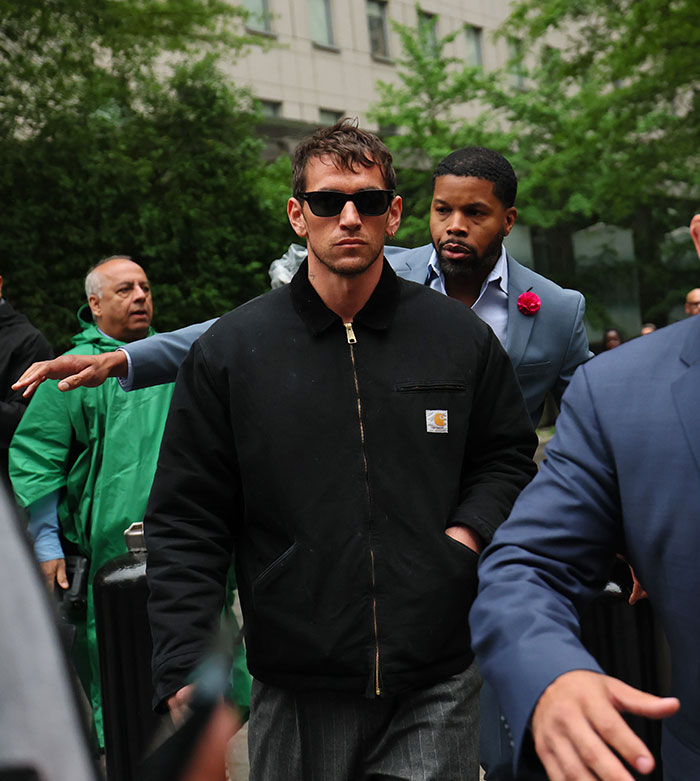 Man in black jacket and sunglasses walking outdoors with security, relating to poured it all over freak-offs and Diddy on stand.