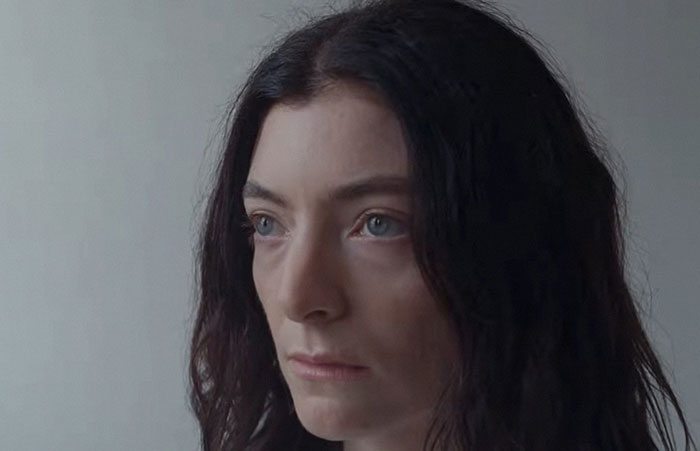 Close-up of a woman with dark hair and blue eyes reflecting on celebrities before their fame in a simple background.