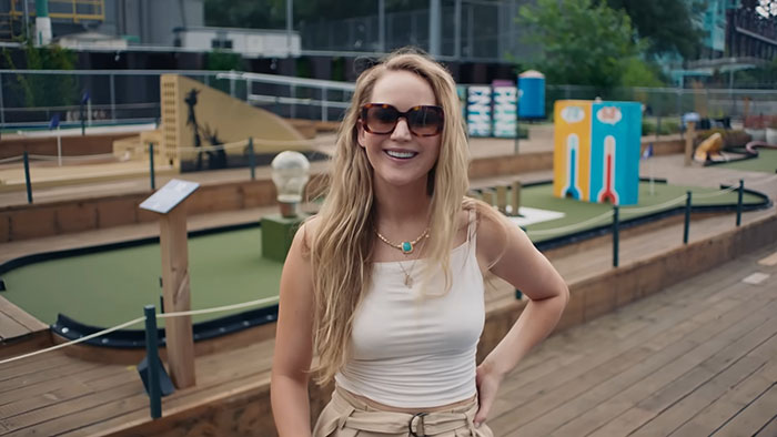 Young woman wearing sunglasses smiles at a mini-golf course, reflecting netizens who knew celebrities before their fame.