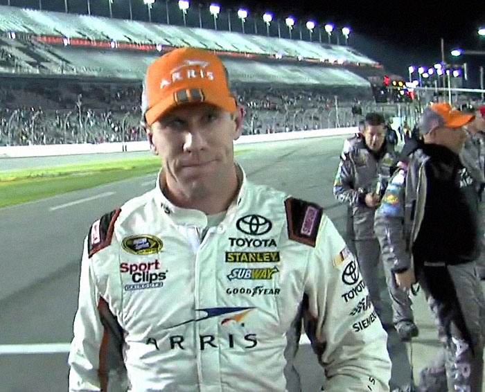 Race car driver in Toyota racing suit and orange cap on track, showcasing celebrities famous before their fame struck.