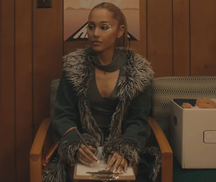 Young woman in a fur-trimmed coat sitting with a clipboard, reflecting a moment before celebrity fame struck.