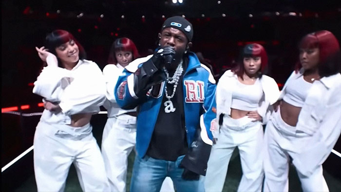 Performer rapping on stage with four dancers in white outfits during a live celebrity performance event.