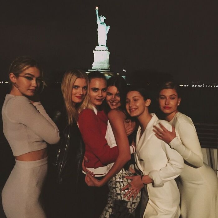 Group of celebrities posing together at night with the Statue of Liberty in the background in a vintage Instagram post.