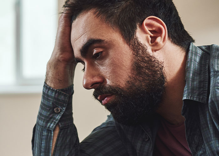 A pensive man with a beard wearing a plaid shirt, reflecting on regrets in a quiet indoor setting about cheating on partners.