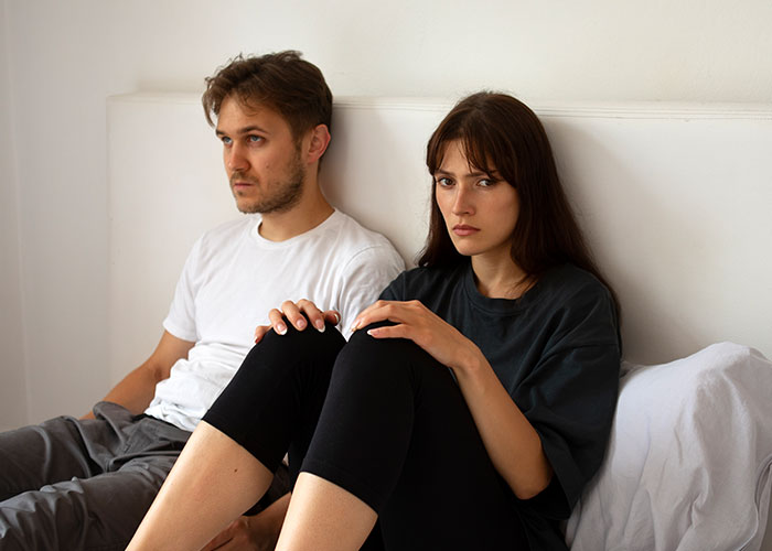 Young couple in a tense moment sitting apart, illustrating emotions related to cheating on their partners and relationship struggles.