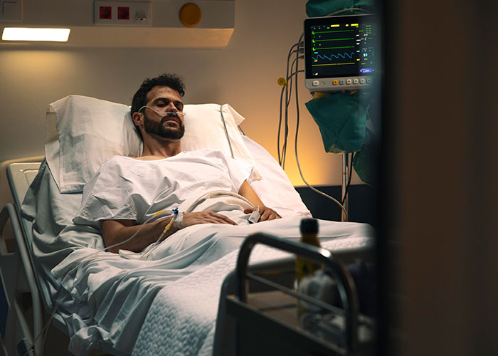 Man in hospital bed with oxygen tube, hooked to heart monitor, representing confessions from people who cheated on partners.