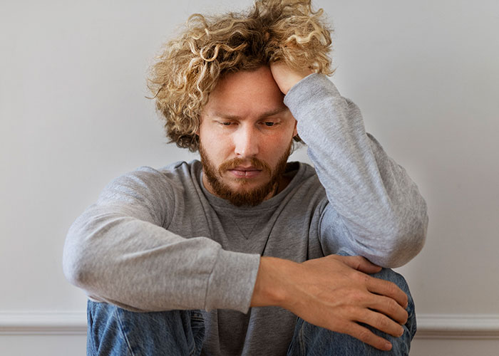 A man with curly hair looking distressed, sitting alone and reflecting on cheating in relationships and confessions.