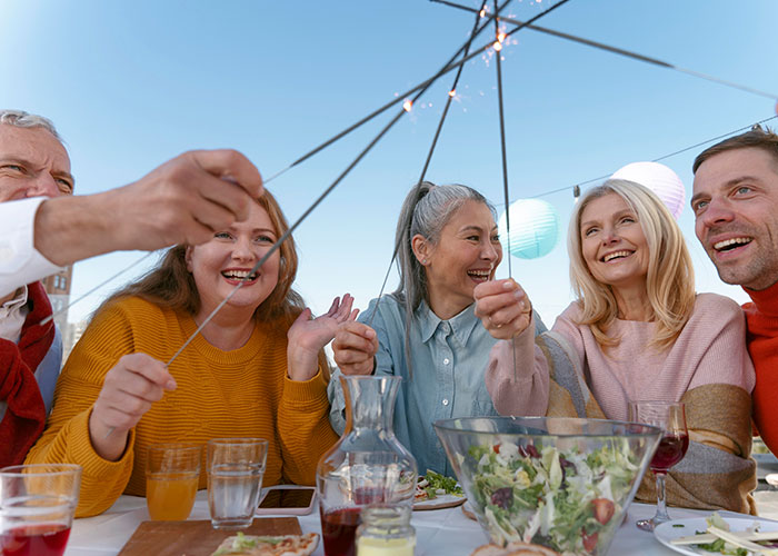 Group of friends smiling and enjoying a meal together while holding sparklers, illustrating confessions of people who cheated.