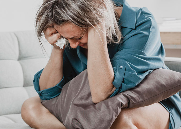 Woman sitting on a couch holding a pillow and crying, expressing emotional pain related to cheating on their partner.