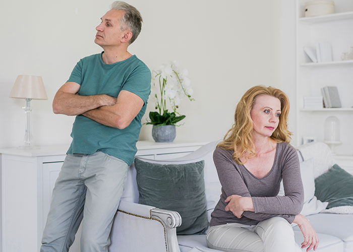 Middle-aged couple in a living room showing tension and distance, reflecting issues related to cheating on their partners.