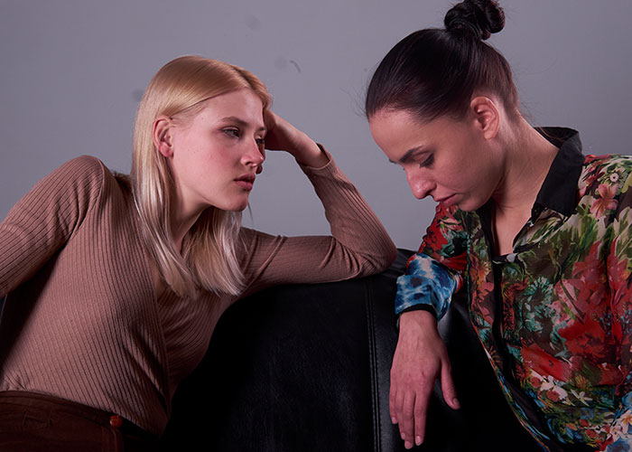 Two women sitting close, appearing upset and reflective, illustrating emotions related to cheating on partners.