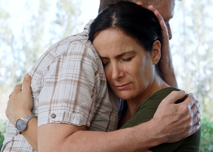 A distressed woman and man embracing outdoors, reflecting emotions related to cheating on their partners confessions.