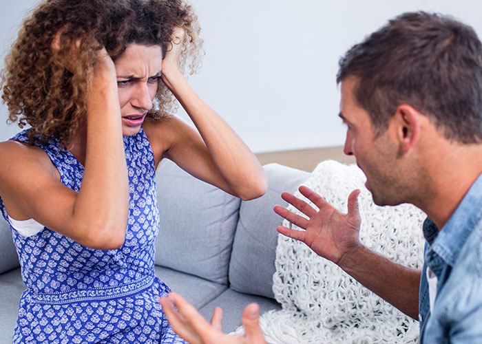 Upset woman holding her head and man arguing on couch, illustrating emotions from people who cheated on their partners.