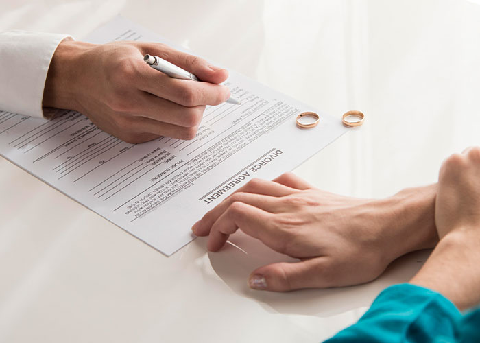Person signing a divorce agreement with wedding rings on the table symbolizing consequences of cheating on partners.