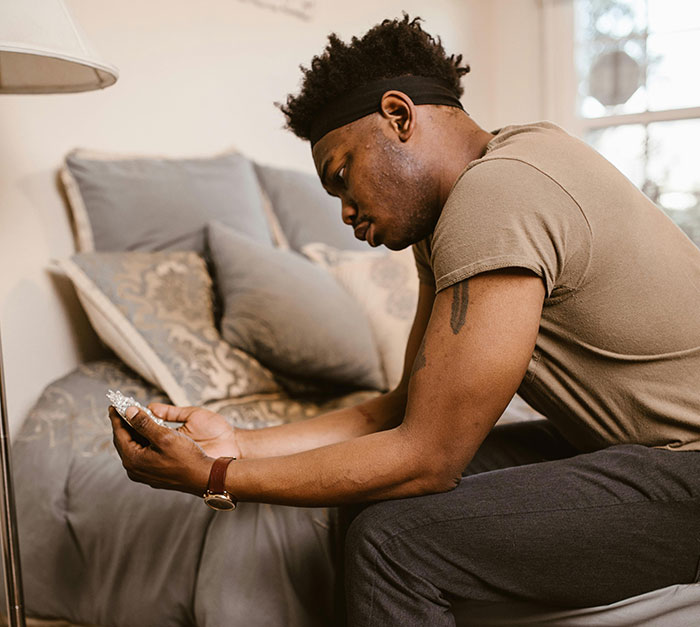 Man sitting on bed looking at phone, reflecting on betrayal and planning his next move after affair revealed. Man sitting on bed looking at phone, reflecting on betrayal and planning his next move after affair revealed.