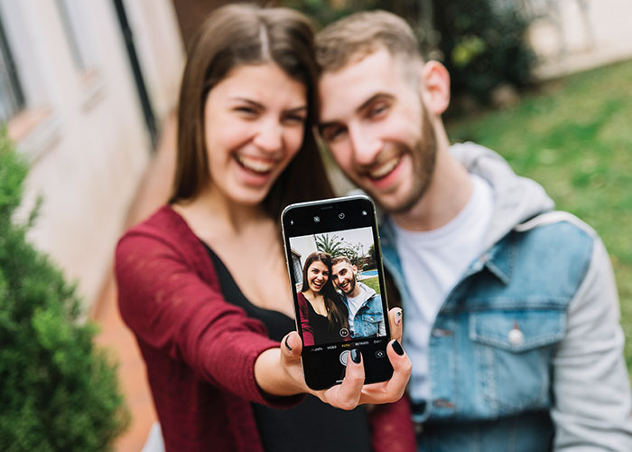 Young couple taking a selfie outdoors, smiling and enjoying a casual moment together, highlighting signs of cheating.