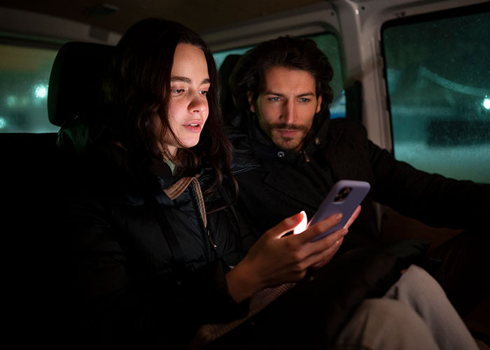 Young couple in a car at night, woman focused on phone displaying possible signs someone is cheating.