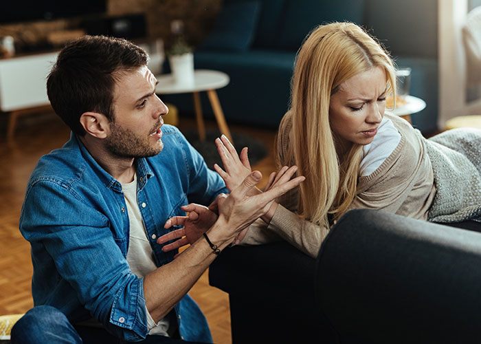 A young couple having an intense argument on a couch showing signs that someone is cheating and trust issues.