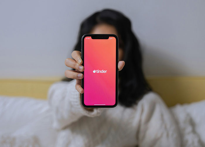 Person holding a phone displaying the Tinder app, illustrating signs someone is cheating and relationship trust issues.