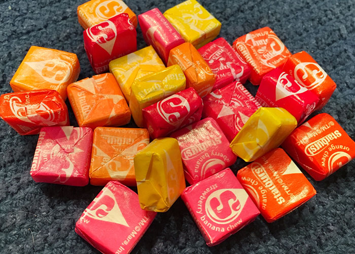 Colorful Starburst candies scattered on a dark textured surface illustrating signs of someone cheating concept.