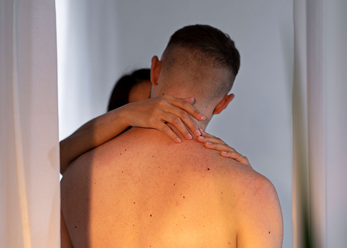A couple embracing intimately behind curtains, illustrating signs that someone is cheating and relationship doubt.