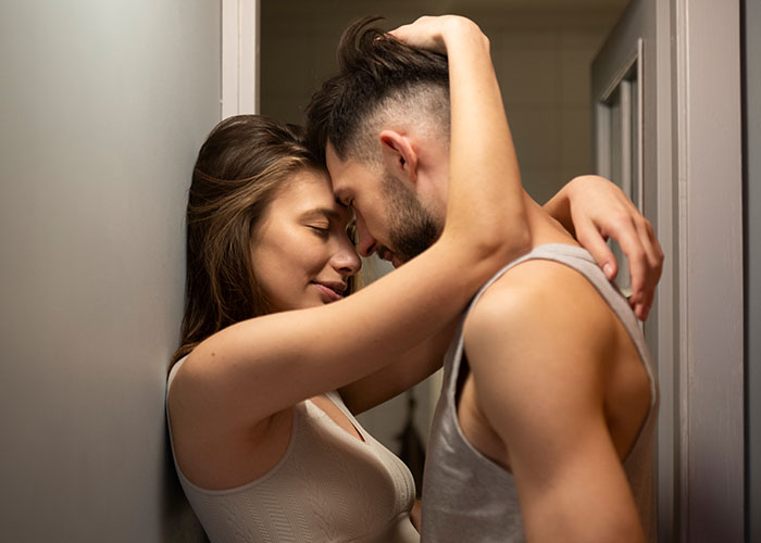Young couple embracing closely in narrow hallway, depicting intimacy and signs someone is cheating in a relationship.