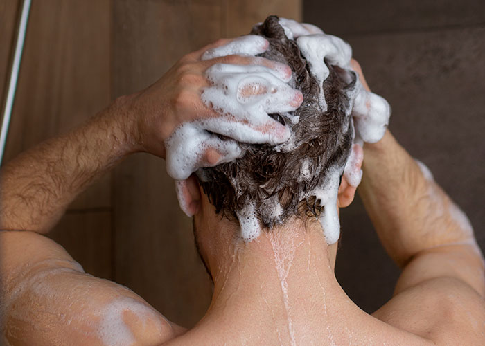 Man washing hair with shampoo in the shower, representing care and reflection on signs of cheating and relationship doubts.