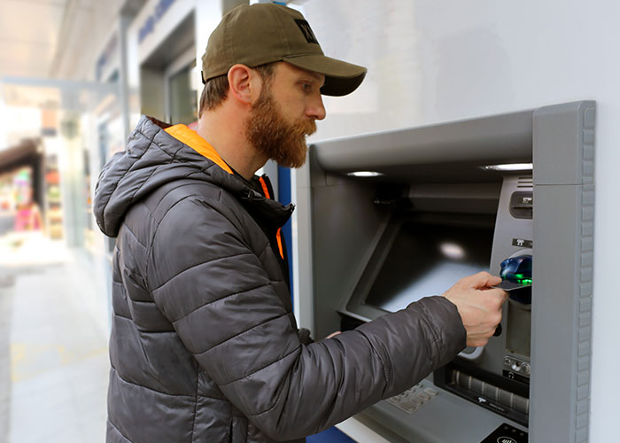 Man in a cap using an ATM outside, illustrating signs that someone is cheating and you’re not just paranoid.