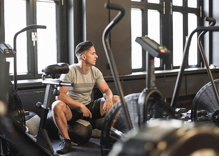 Young man sitting on a medicine ball in a gym, reflecting on signs that someone is cheating and relationship trust issues.