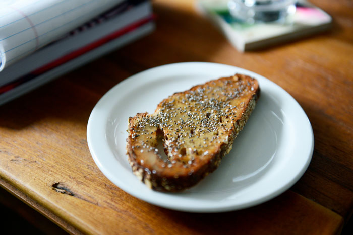 Slice of toasted bread topped with spread and sprinkled with chia seeds on a white plate on wooden table Slice of toasted bread topped with spread and sprinkled with chia seeds on a white plate on wooden table