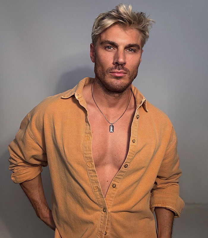 Blond man with styled hair wearing an unbuttoned shirt and necklace, related to Kim Kardashian's hair stylist in Cannes. Blond man with styled hair wearing an unbuttoned shirt and necklace, related to Kim Kardashian's hair stylist in Cannes.
