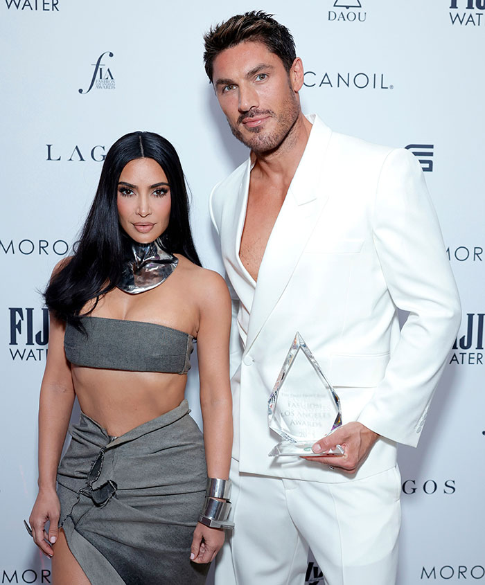 Kim Kardashian with her hair stylist posing at an event, hairstylist wearing white suit holding an award. Kim Kardashian with her hair stylist posing at an event, hairstylist wearing white suit holding an award.