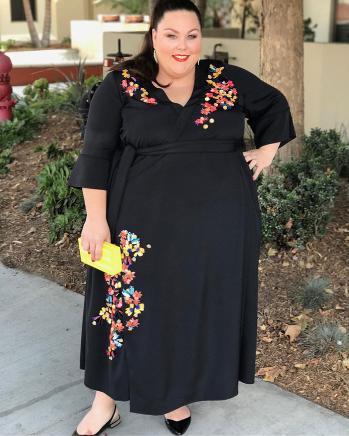 Chrissy Metz smiling outdoors in a black floral dress showing her slimmed-down look after 100lbs weight loss.