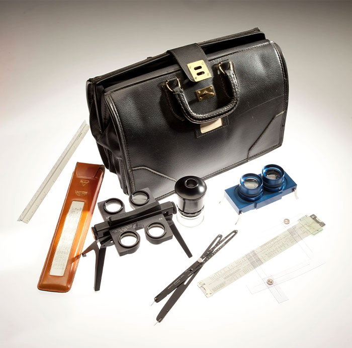Set of vintage CIA spy technology equipment including optical devices and measuring tools beside a black leather briefcase.
