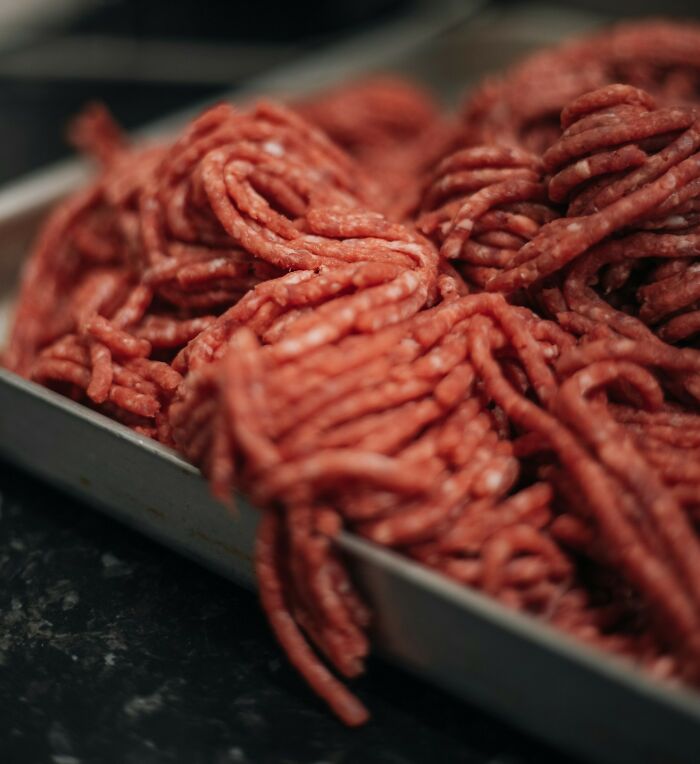 Close-up of raw ground meat in a metal tray, illustrating a company secret about food handling or processing practices.