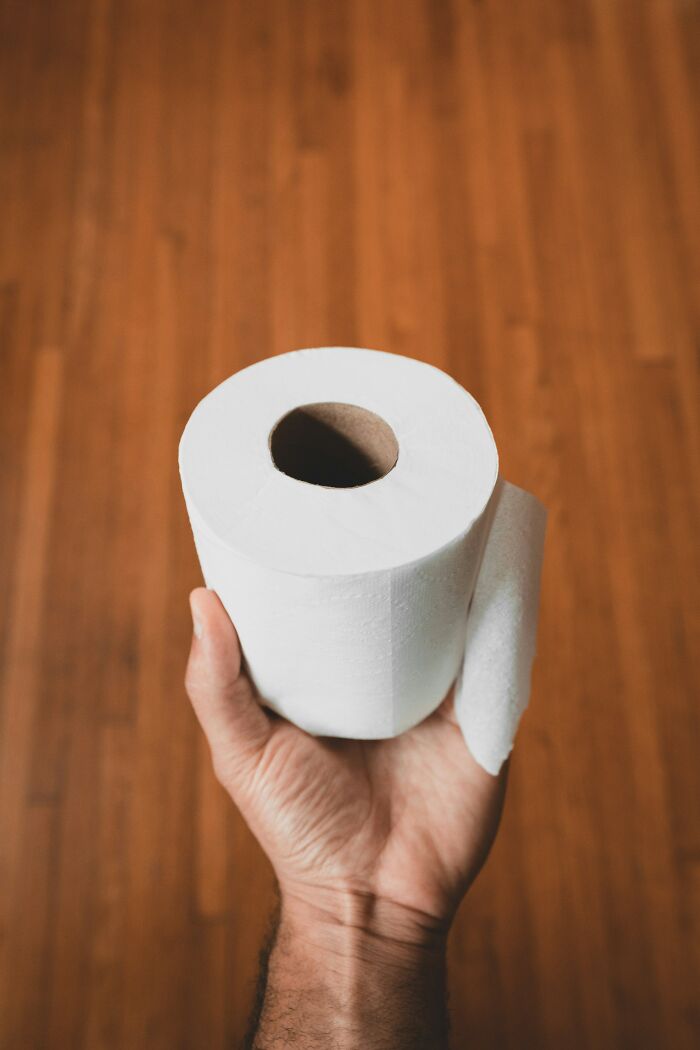 Hand holding a roll of toilet paper against a wooden floor, illustrating mundane things that make people sick.