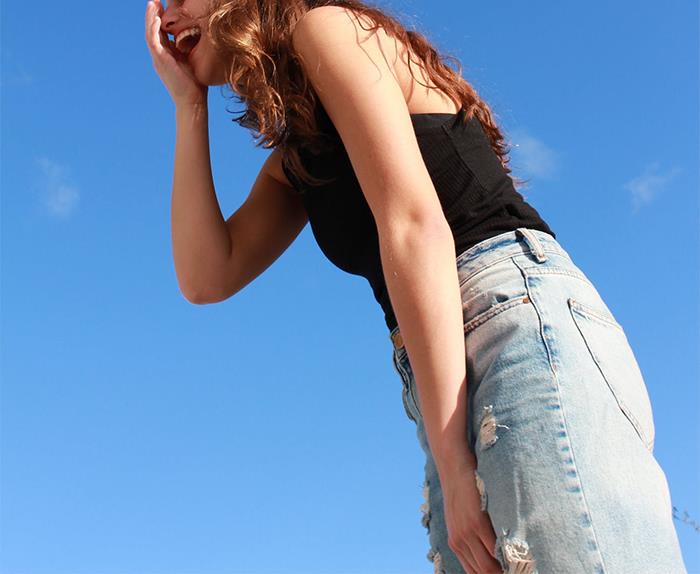 Young woman in black top and ripped jeans laughing outdoors under clear blue sky, symbolizing dark family secrets revealed.