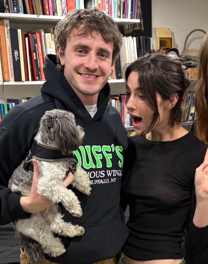 Two people and a dog indoors with bookshelves in the background, sharing a moment related to celebrity gossip.