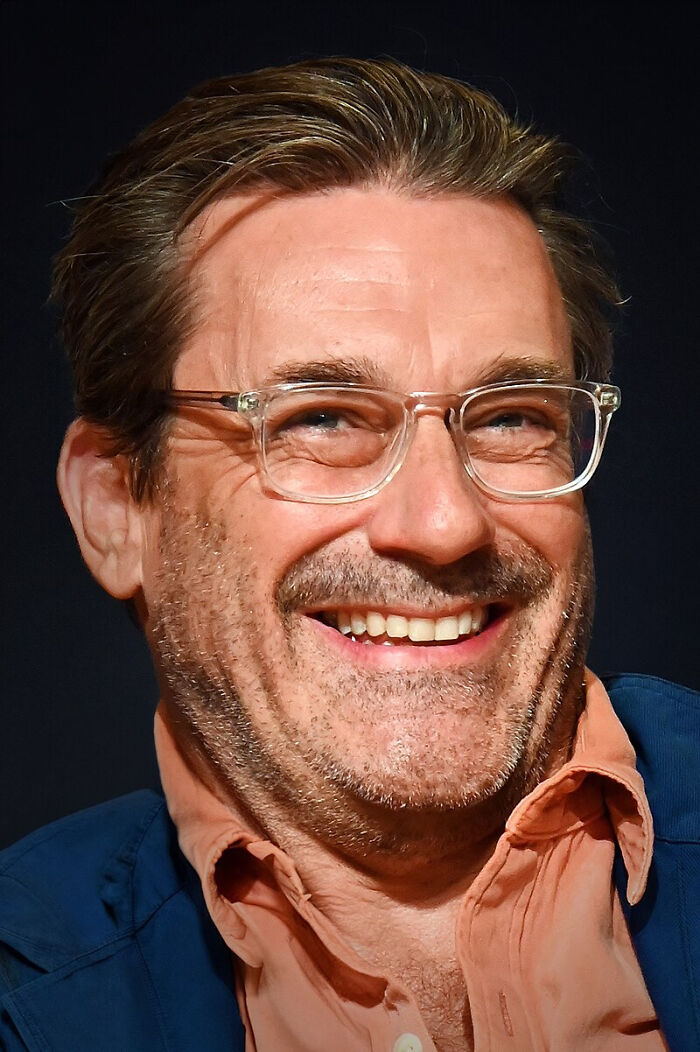Smiling man wearing clear glasses and a blue jacket, capturing a candid moment related to celebrity gossip and tea.