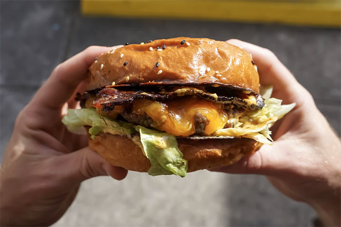 Close-up of a cheeseburger held by hands, illustrating a funny national stereotype about food culture.
