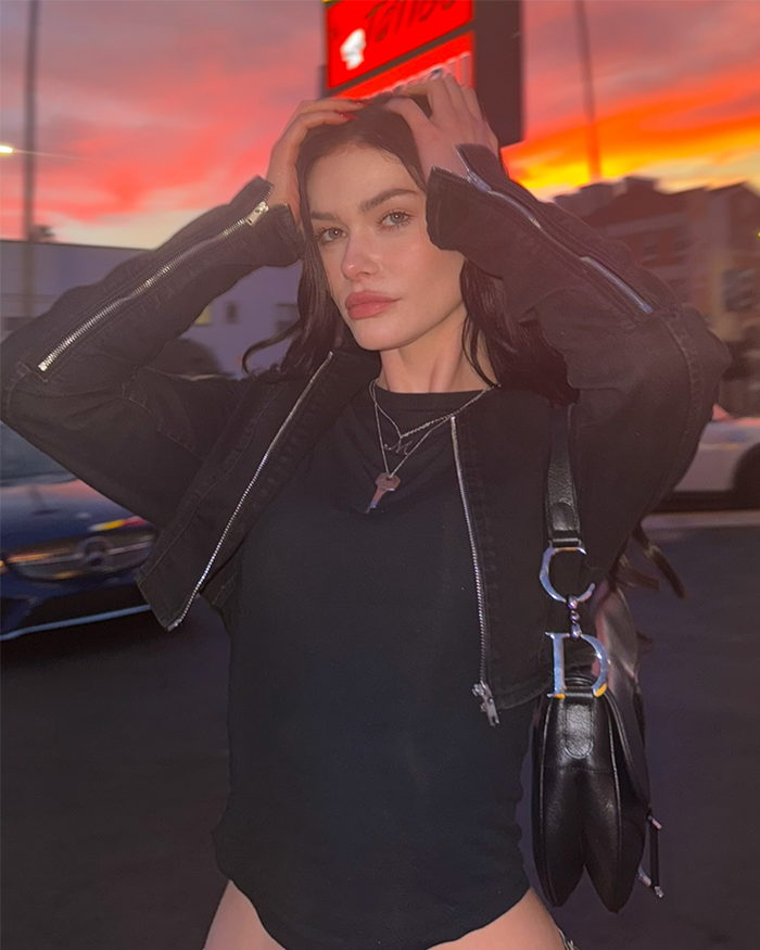Young woman posing outdoors at sunset, wearing a black jacket and necklace, capturing massive praise in a viral clip.