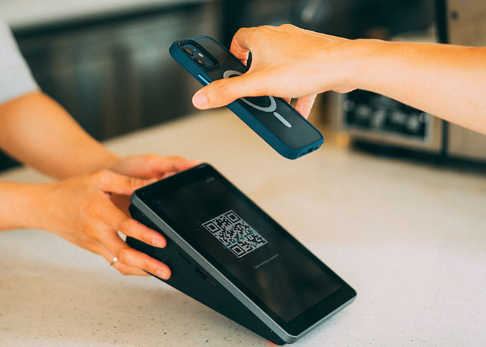Person using mobile phone to scan QR code on a payment terminal illustrating national stereotypes about technology use.