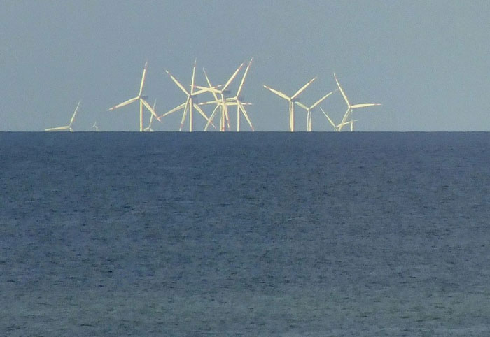 Wind turbines appearing on the horizon over the ocean, related to craziest conspiracy theories on the internet.