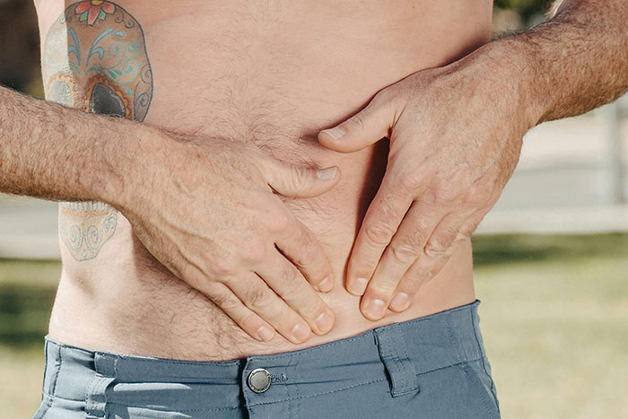 Man with tattoo holding lower abdomen in pain outdoors, illustrating DIY medical treatments gone wrong risks.