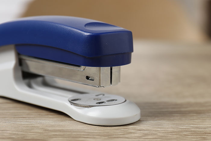 Close-up of a blue and white stapler on a wooden surface, symbolizing DIY medical treatments gone horribly wrong.