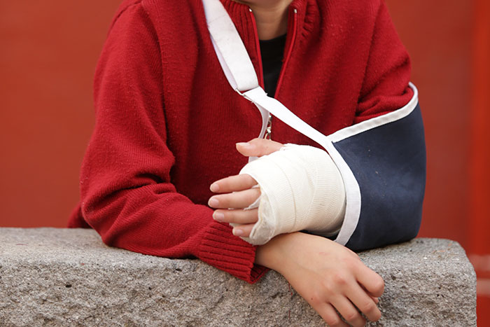 Person wearing a red sweater with a heavily bandaged arm in a sling, showing consequences of DIY medical treatments gone wrong.